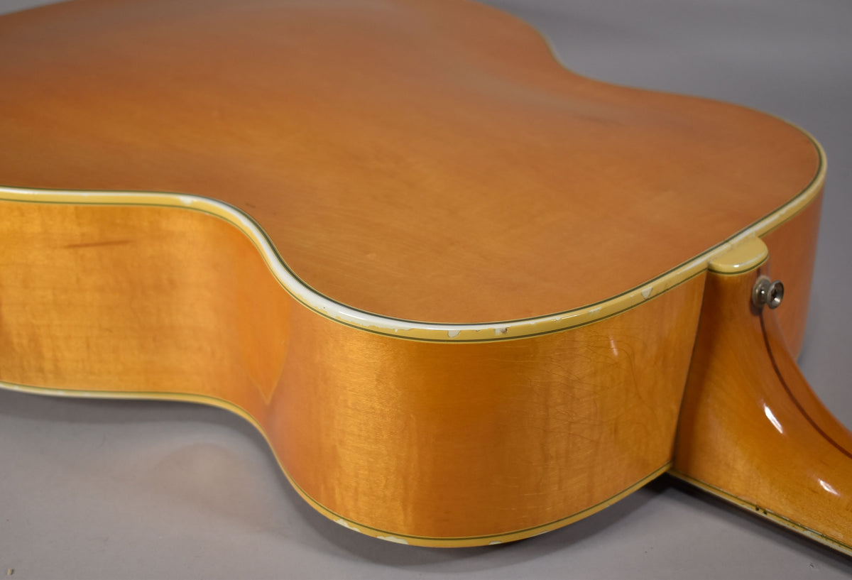 The lower bout and waist of a blonde acoustic guitar, showing finish wear and chips along the white binding.