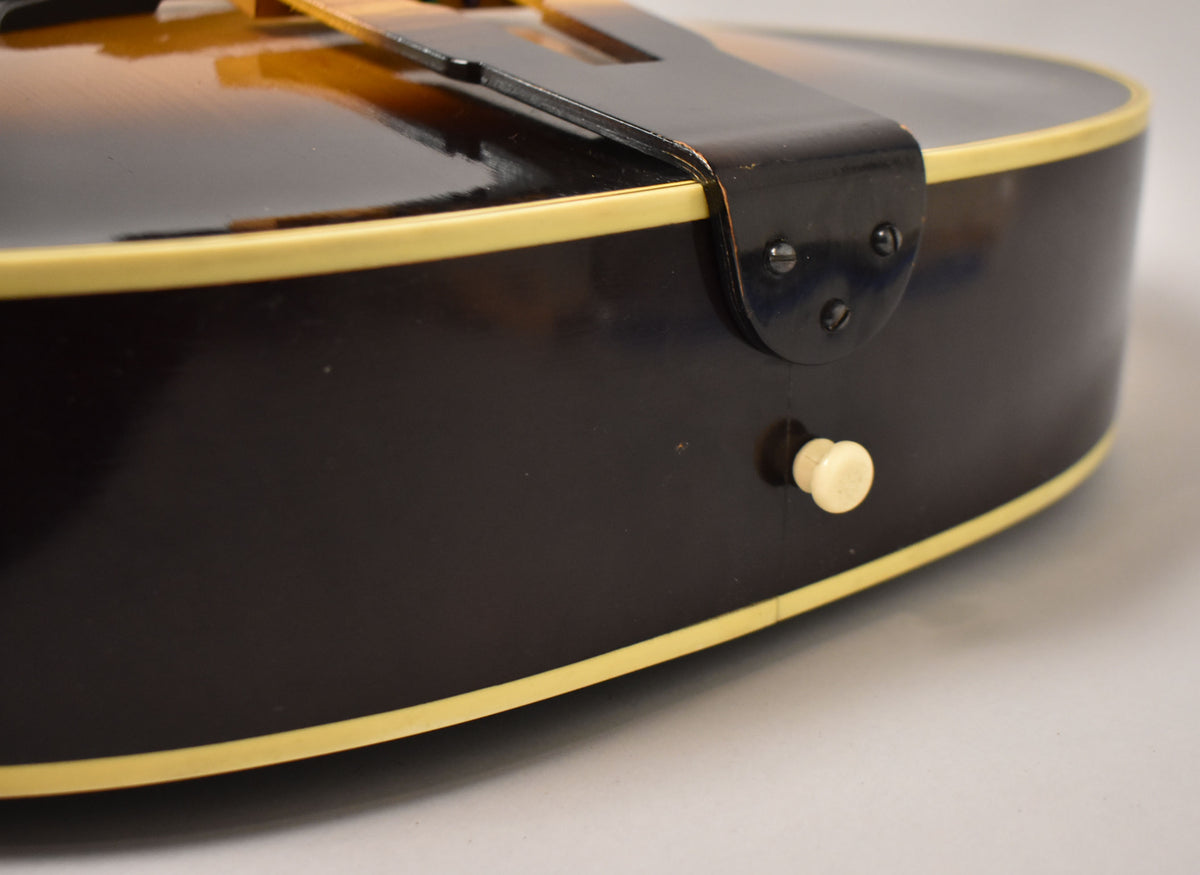 Close-up of the guitar's lower bout, showing the dark brown sides with cream binding, a black tailpiece, and a single cream strap button.
