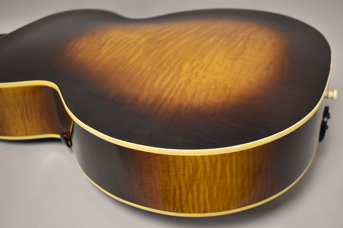 The guitar's lower bout and side, showing a sunburst finish with flame maple grain and cream binding, plus a white endpin jack.