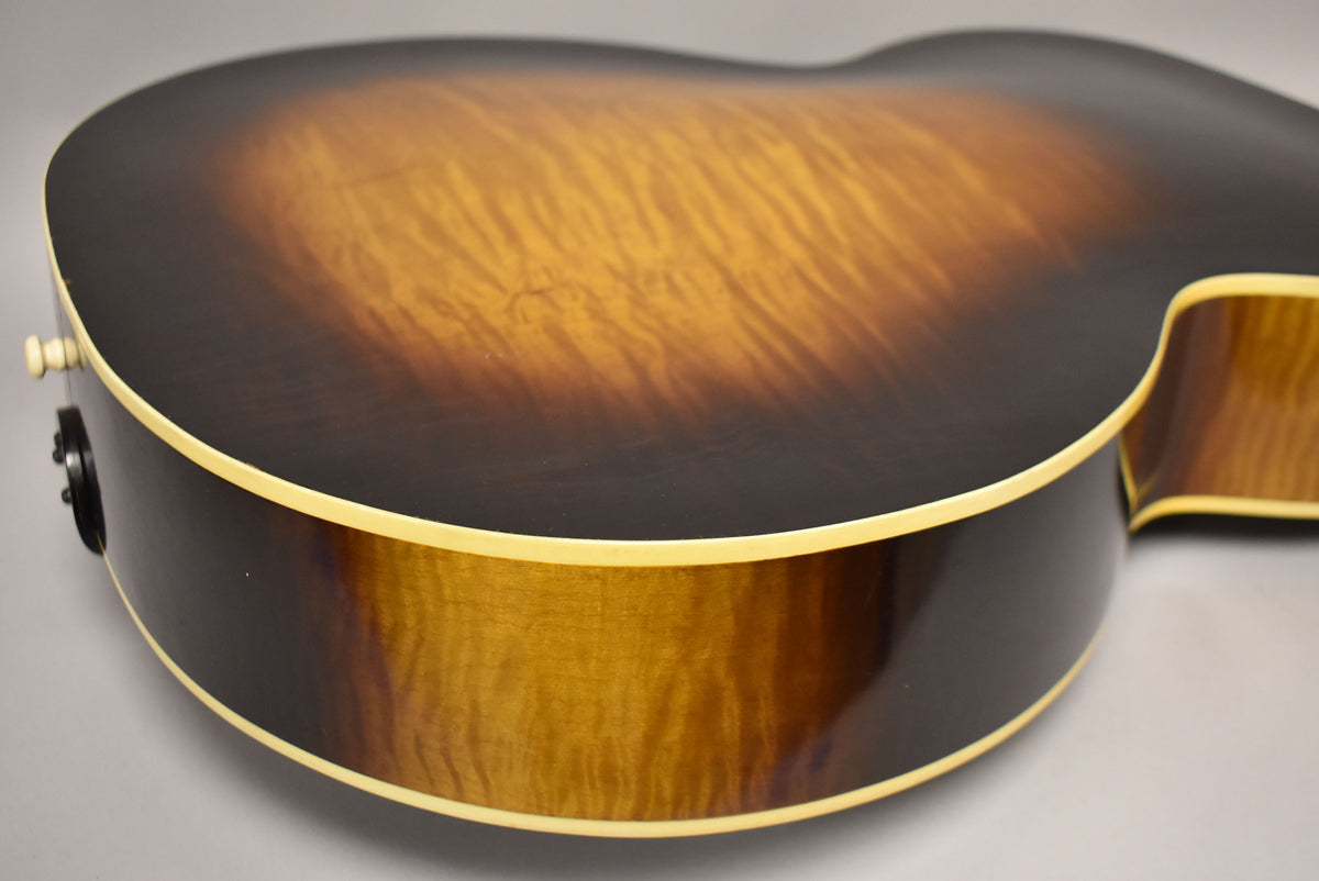 Close-up of the guitar's lower bout, showing the sunburst finish with flame maple grain and cream binding, with a strap button.