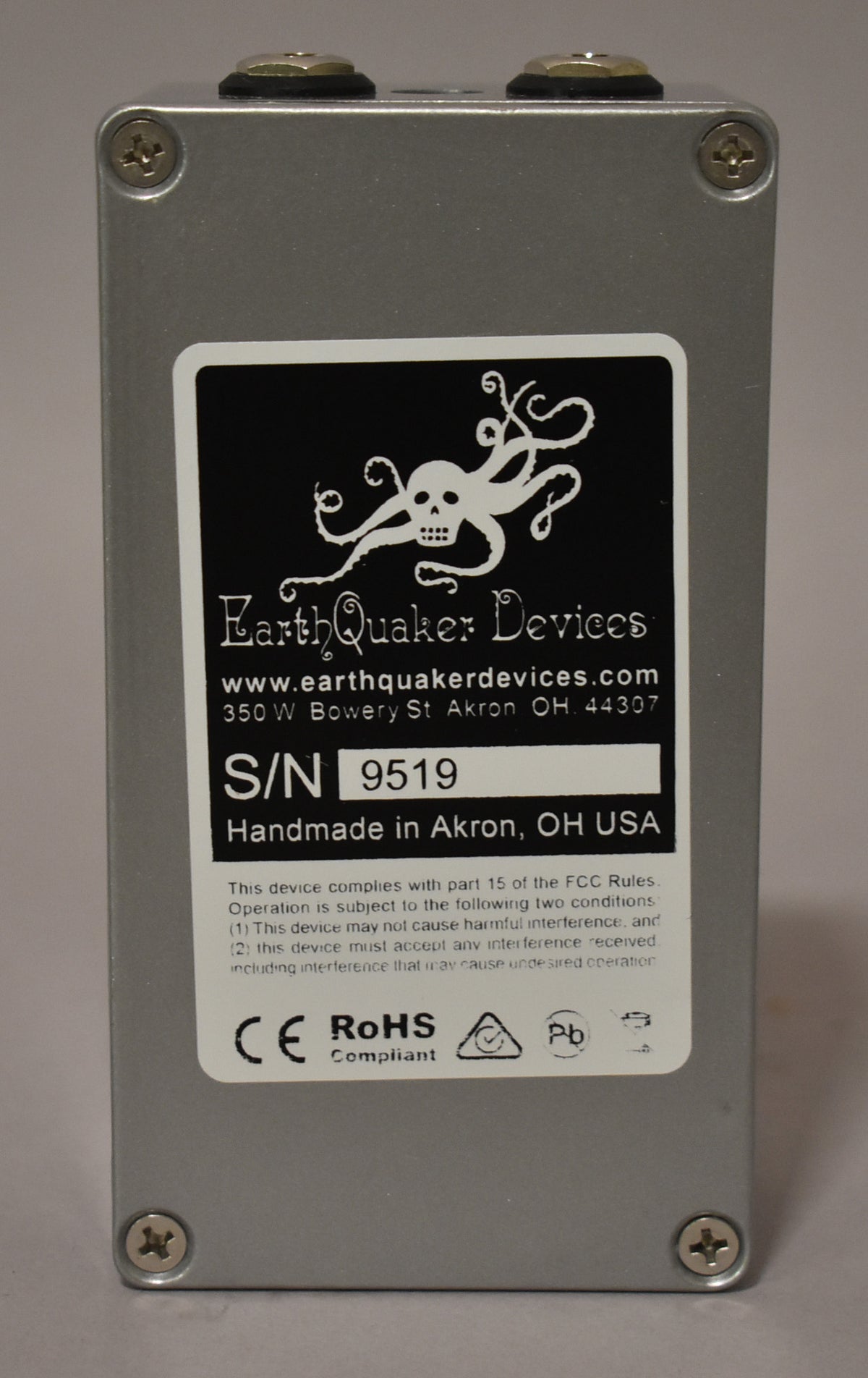 The pedal's silver-grey back panel is shown, with a large black and white sticker displaying a skull-octopus logo and serial number.