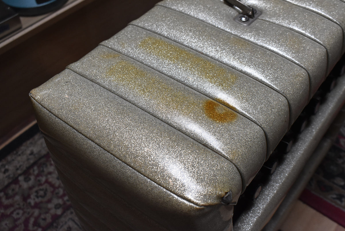 Close-up of the silver sparkle tuck-and-roll top of the amp, showing two large brown stains and a small tear on the front edge.