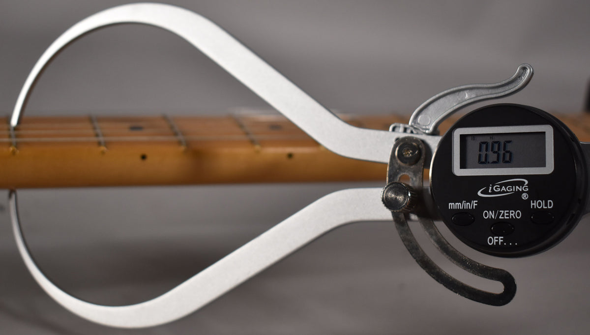 A digital caliper measures the maple fretboard and frets, displaying "0.96" on its screen.