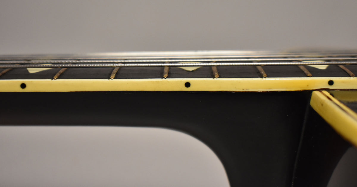 Close-up of the guitar's dark fretboard and neck, showing cream binding, trapezoid inlays, and some wear on the frets.