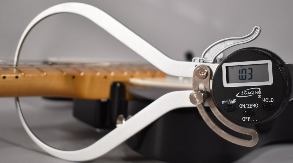 Close-up of the guitar's maple neck and fretboard, with a digital caliper measuring the string height at 1.03mm.