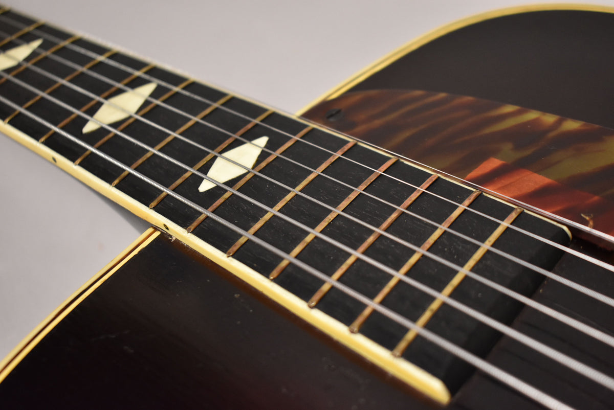 Close-up of the dark fretboard with diamond inlays, showing light wear on the frets and a tortoiseshell pickguard.
