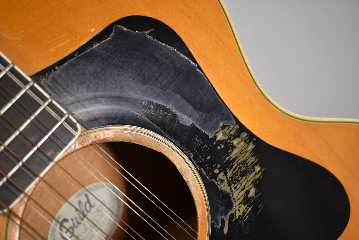 Close-up of the natural blonde body and soundhole, showing significant wear and peeling on the black pickguard.