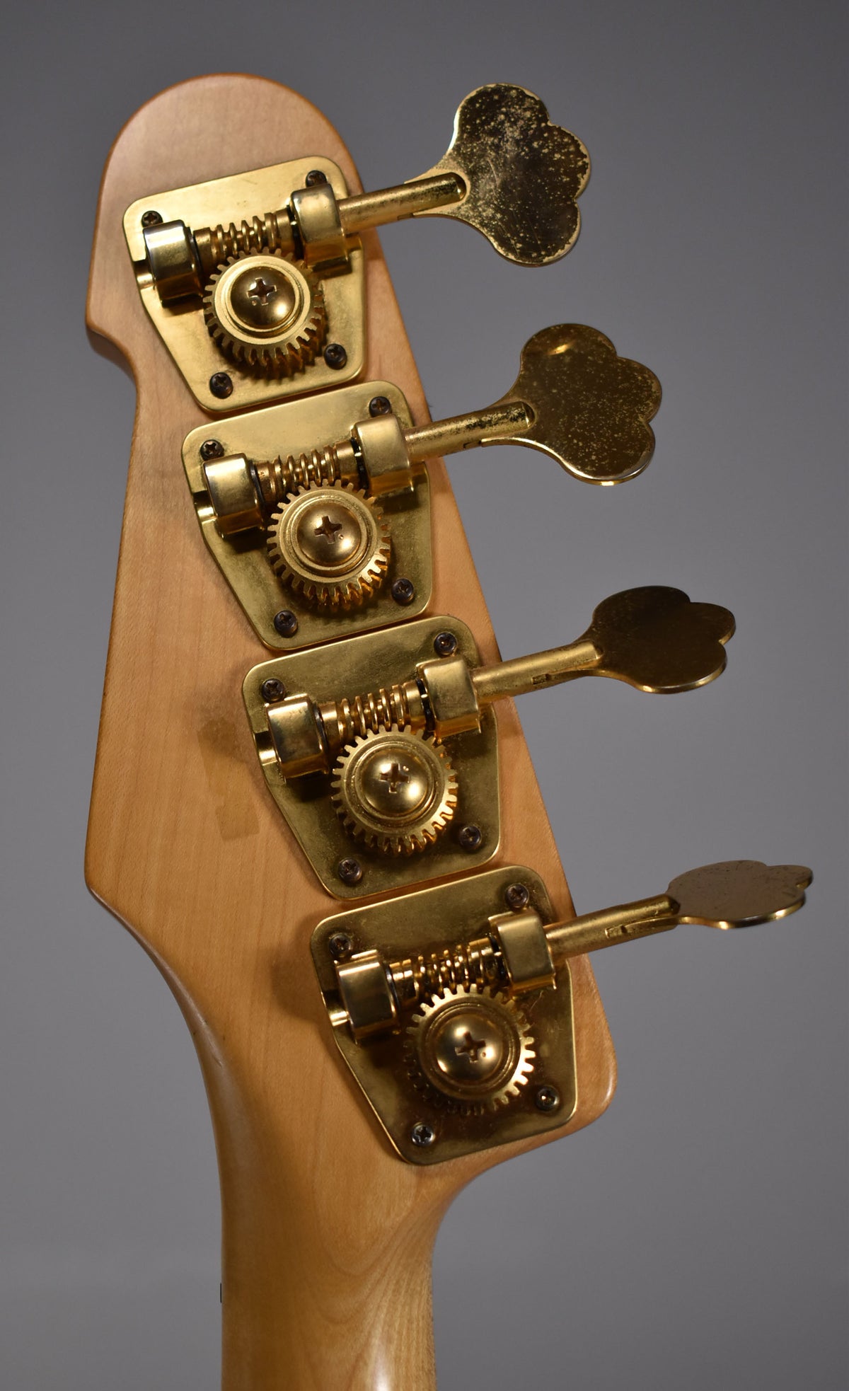 Close-up of the bass headstock from behind, showing four gold-plated tuners with cloverleaf keys and visible tarnishing.