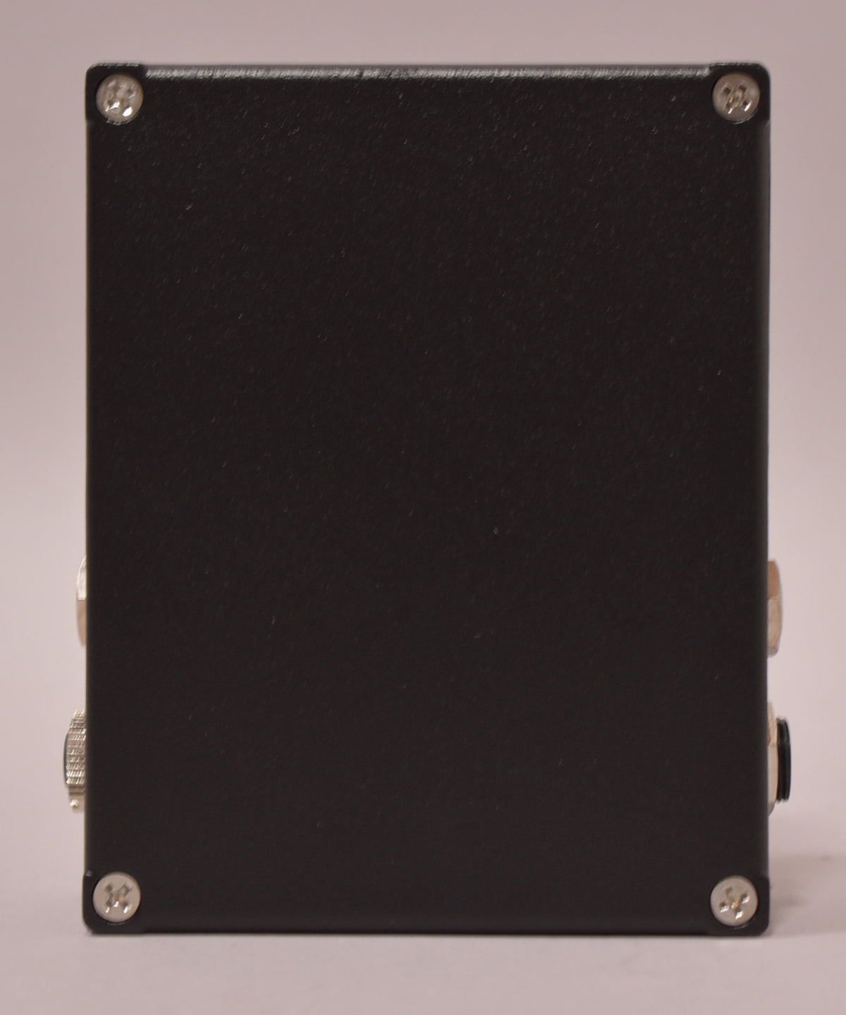 Side view of a black effect pedal with four visible screws and two silver-colored jacks on the left side.