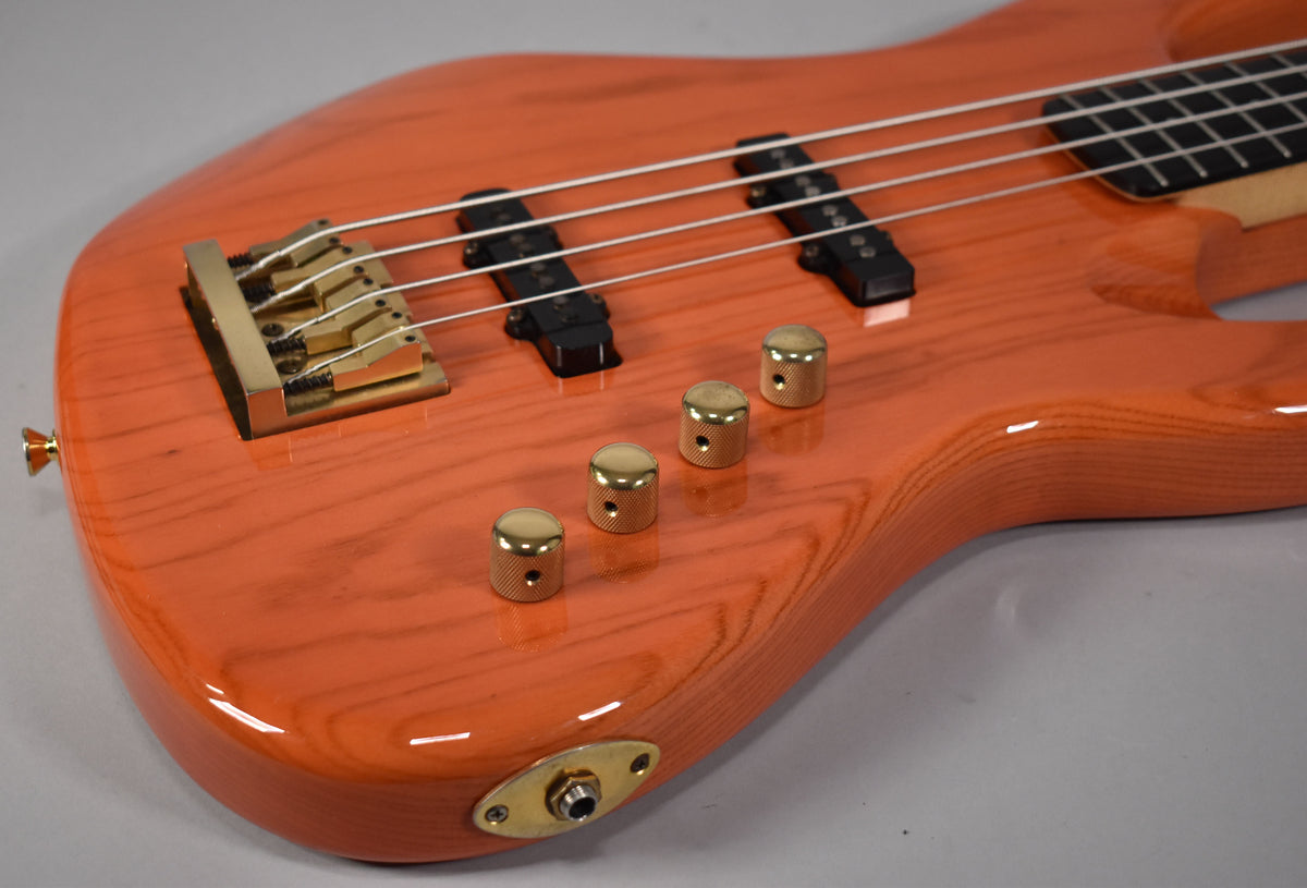 Close-up of the translucent orange bass body, showing the brass bridge, four knurled brass control knobs, and two black pickups.