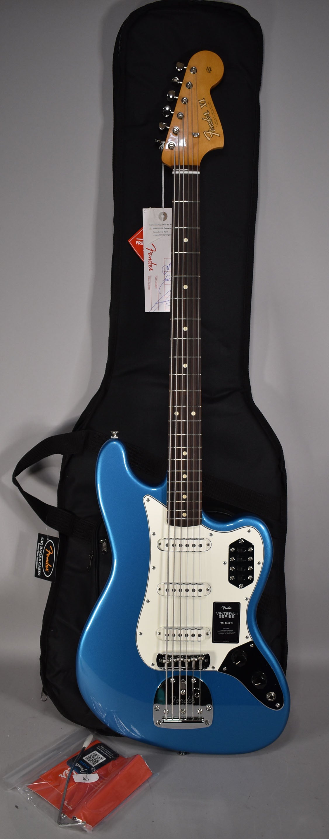 Full-length view of a glossy Lake Placid Blue Bass VI with a white pickguard, three single-coil pickups, and four black slider switches.