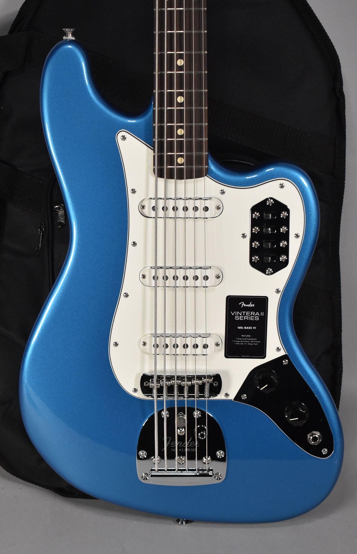 A full-frame view of a metallic blue Bass VI with a white pickguard, three single-coil pickups, and a chrome vibrato tailpiece.