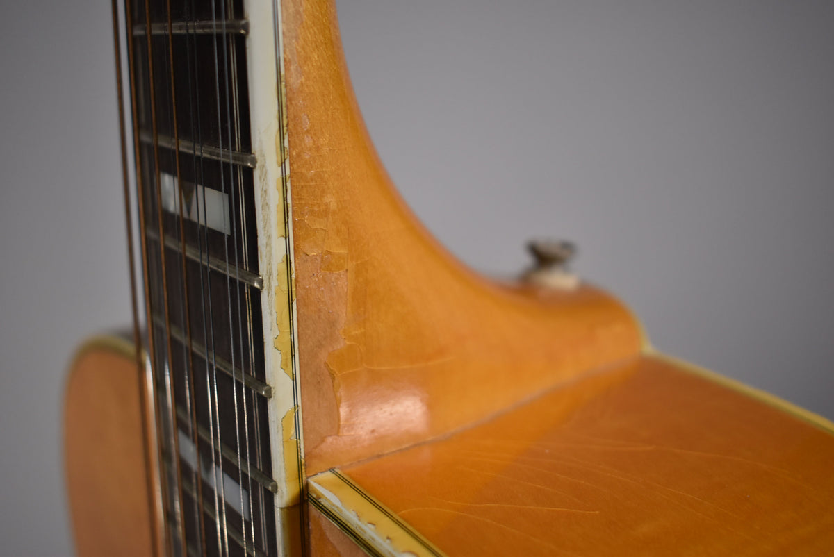 Close-up of the guitar's blonde neck heel and body, showing significant finish checking and wear along the binding and neck.