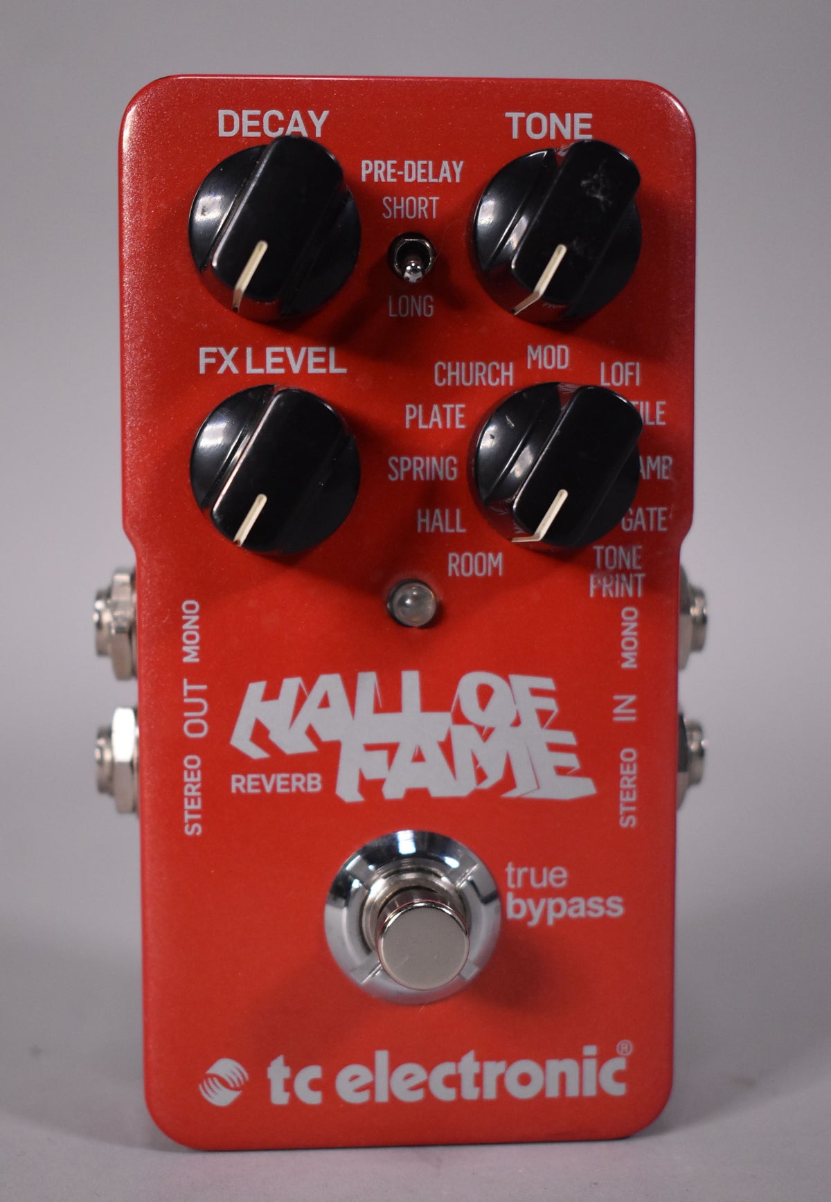 A top-down view of a rectangular, metallic red pedal with four black knobs, a chrome footswitch, and two small toggle switches.