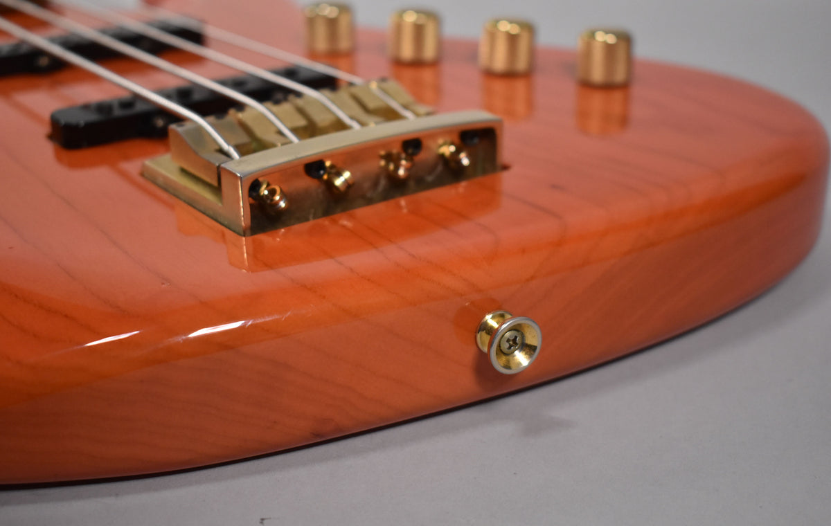 Close-up of the translucent orange bass body, showing the gold bridge, four gold control knobs, and a gold strap button with minor wear.