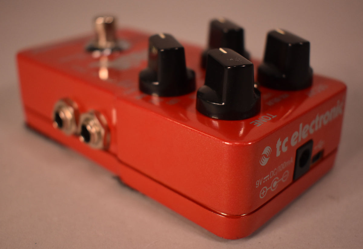 Red metallic pedal, angled from the left, showing four black control knobs, two input jacks, and a power input on the right side.