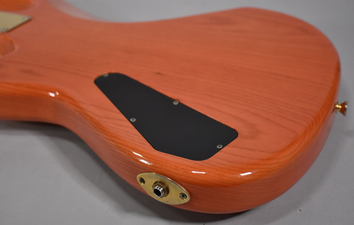 The translucent orange bass body, viewed from the back, shows a black control cavity cover and a gold output jack plate.