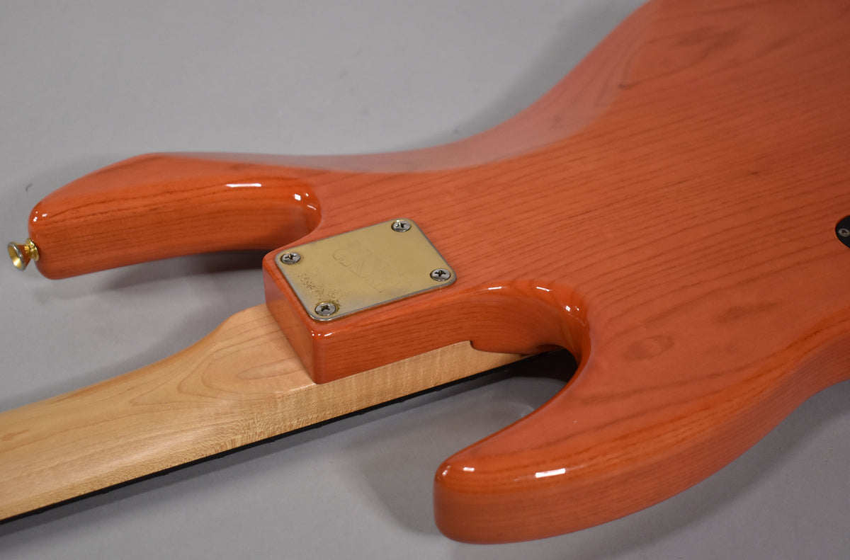 The bass's translucent orange body, showing wood grain, curves around a light maple neck with a worn gold neck plate.