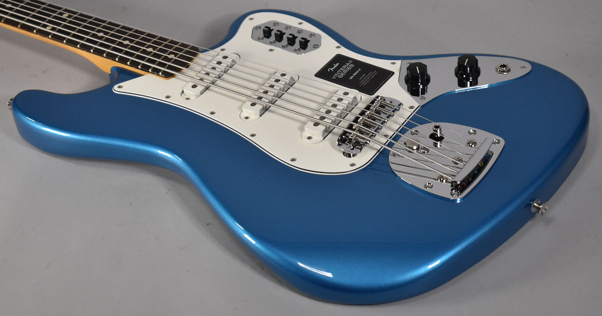 The Lake Placid Blue Bass VI is angled from the upper left, showing its glossy body, white pickguard, chrome hardware, and six strings.