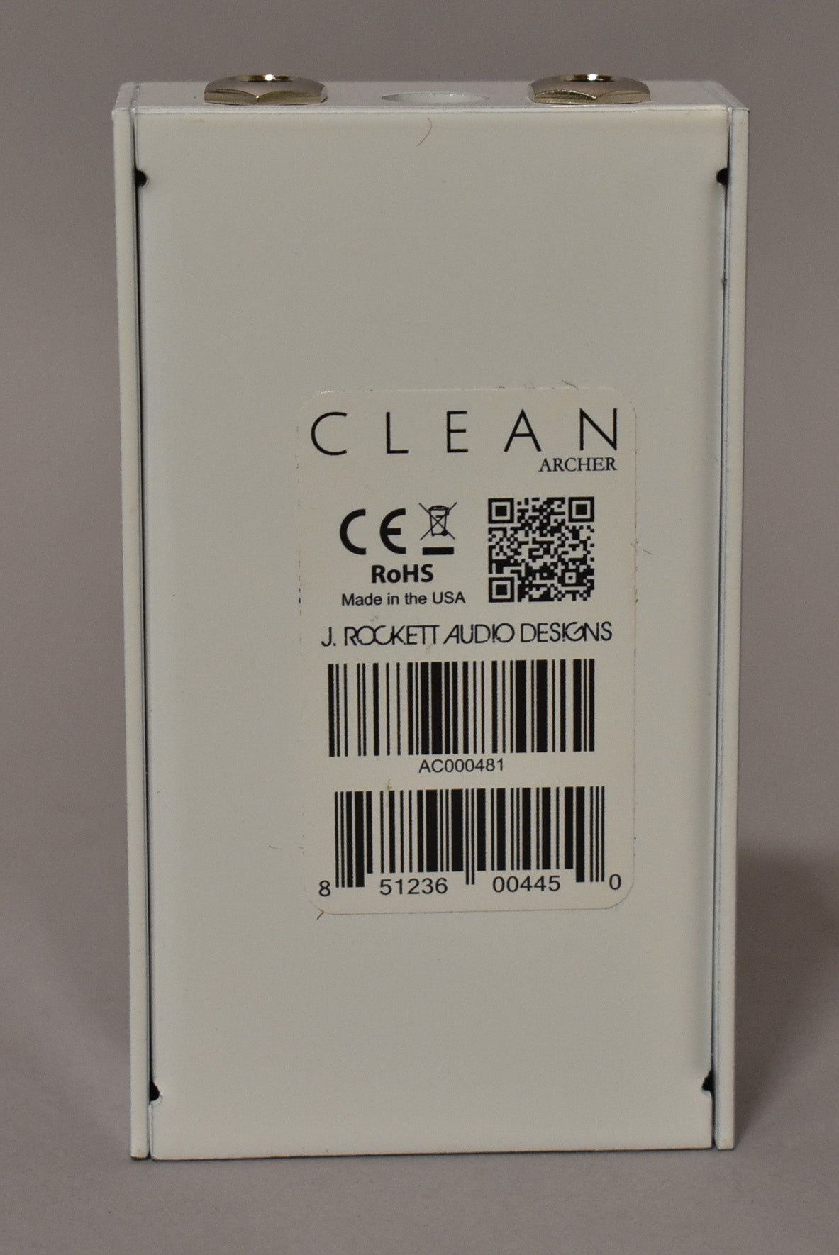 The white effect pedal is viewed from the back, showing a large label with barcodes and regulatory marks, and two silver jacks on top.
