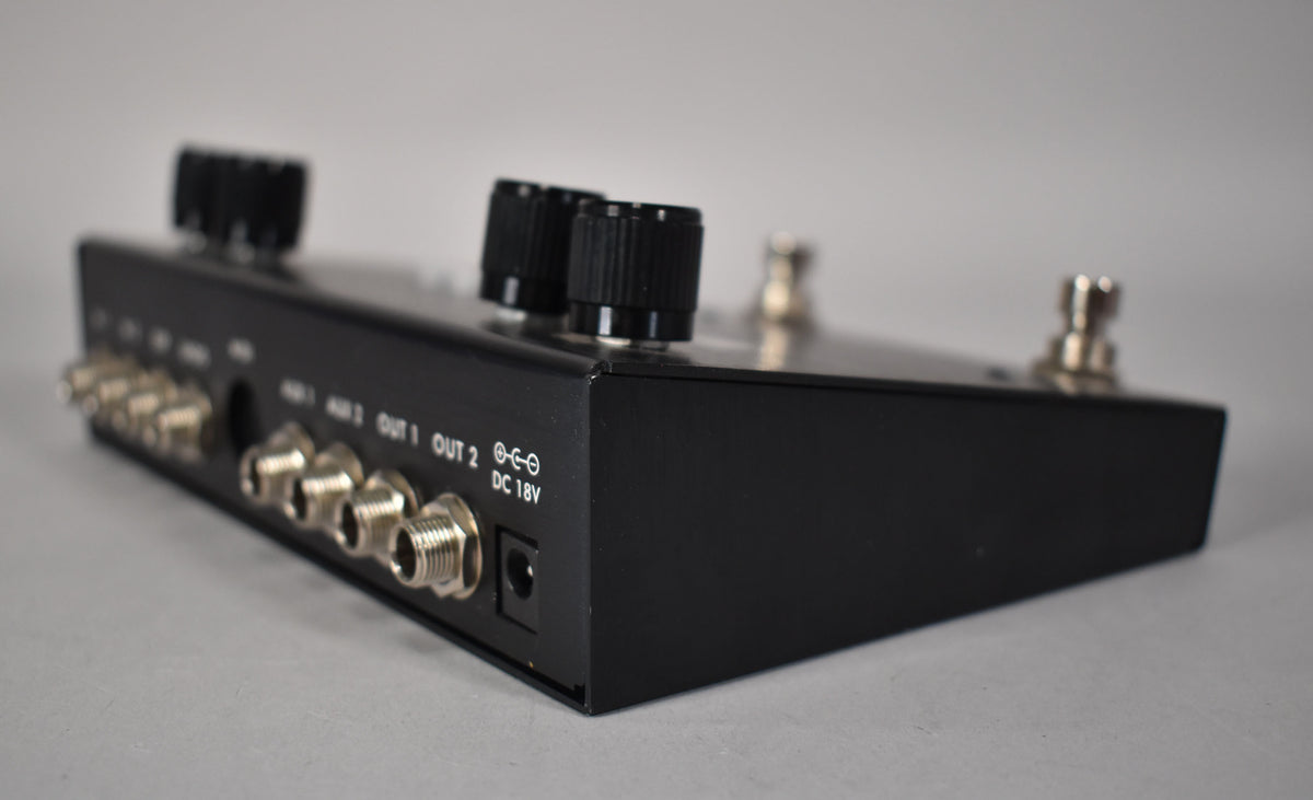 A black metal pedal, viewed from the rear left, showing multiple silver input/output jacks and a DC 18V power input.