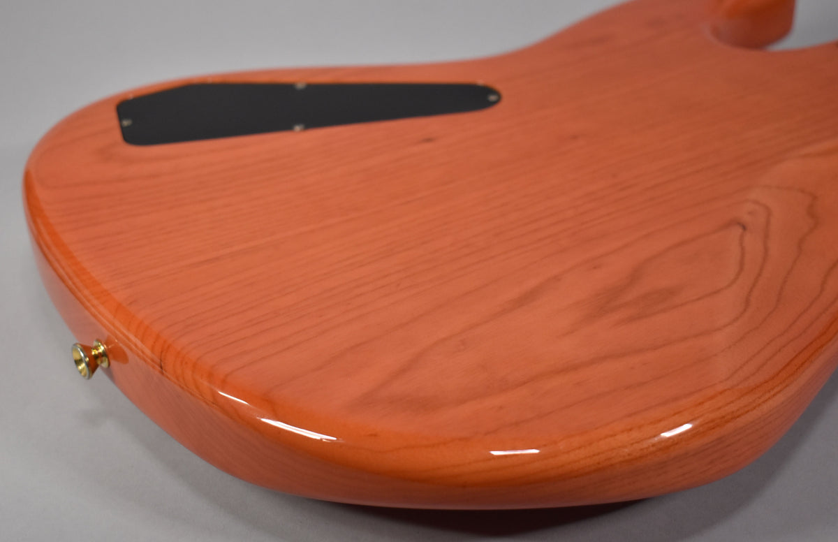 The bass body's translucent orange finish reveals wood grain, with a black control cavity cover and a gold strap button on the lower bout.
