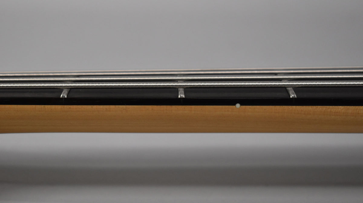 Close-up of the bass neck from the side, showing the light wood neck, dark fretboard, frets, and four strings.