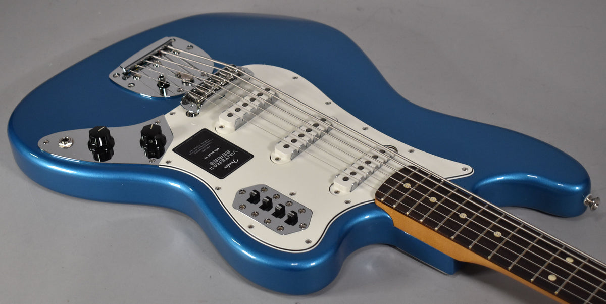 The metallic blue Bass VI is angled from the upper left, showing its white pickguard, three single-coil pickups, and chrome hardware.