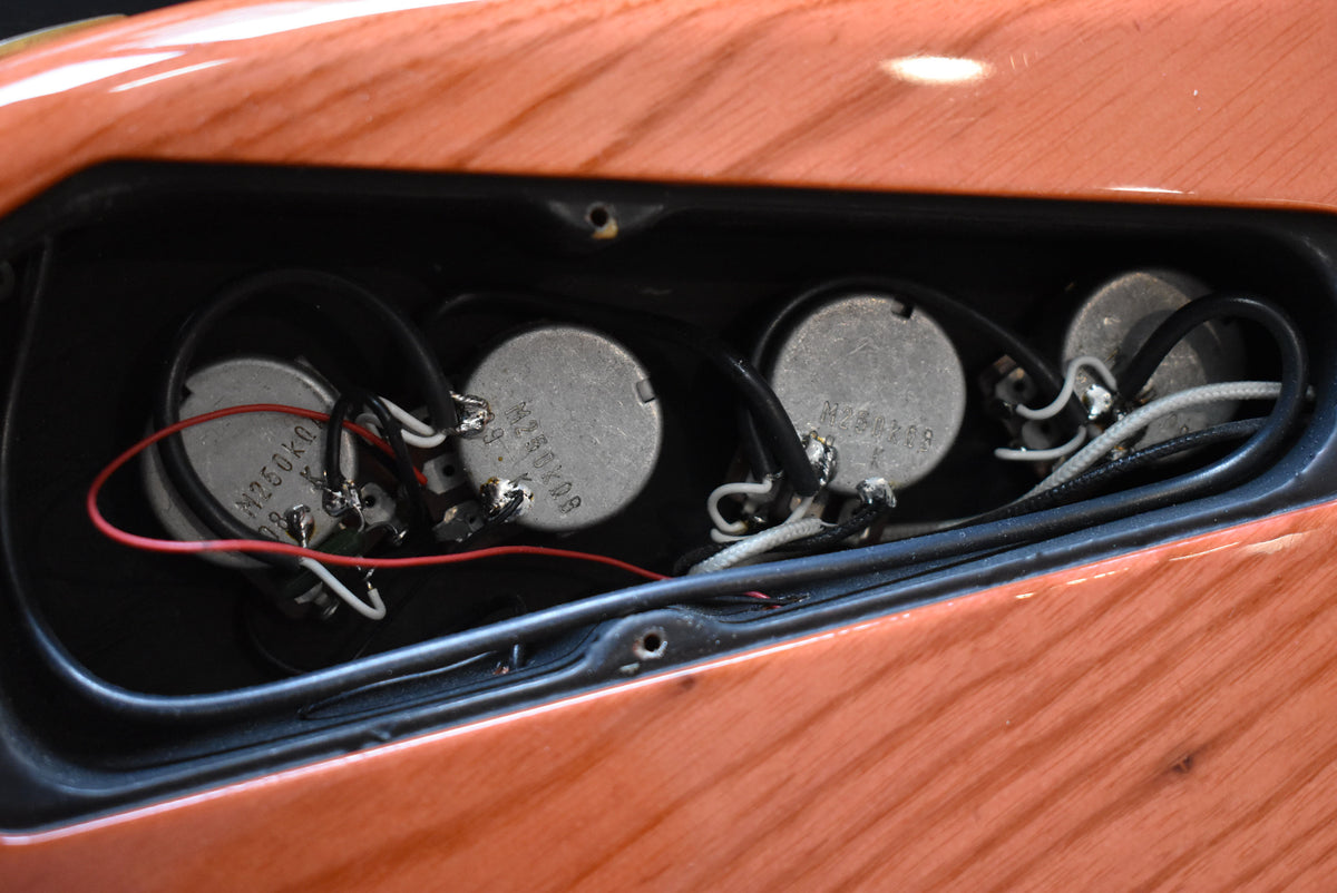 Close-up of the bass's control cavity, revealing four silver potentiometers with soldered wires, set into the translucent orange body.