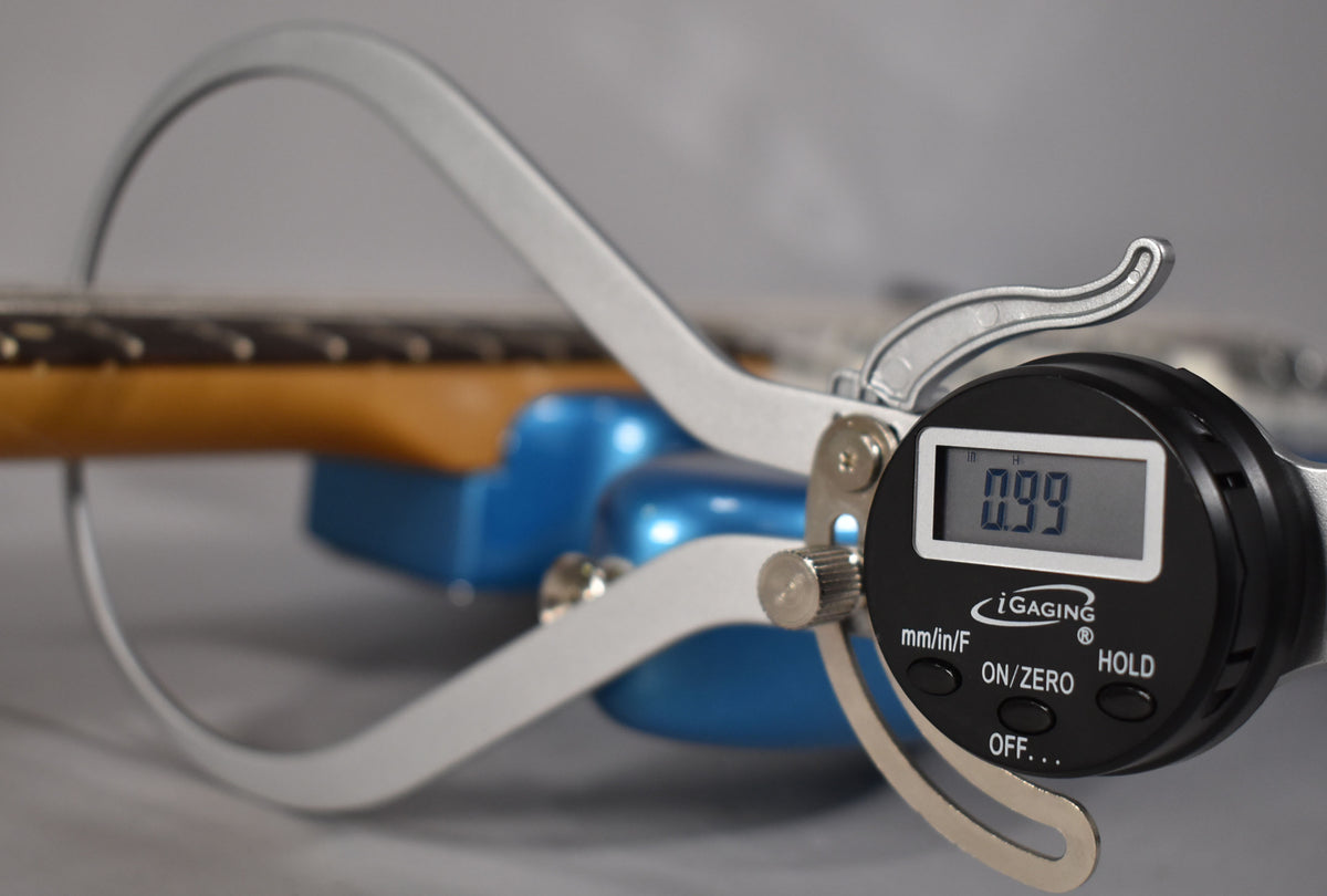 A digital caliper measures the neck thickness of the Lake Placid Blue Bass VI, showing 0.99 on its display.