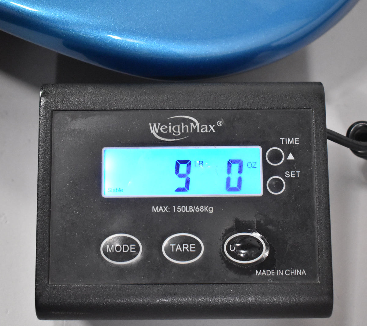 Close-up of a digital scale displaying "9 LB 0 OZ" in blue, with a Lake Placid Blue bass body partially visible above.