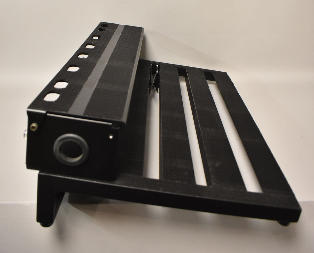The black pedalboard is angled, showing its slatted surface, a row of circular holes, and a large circular port on the side.