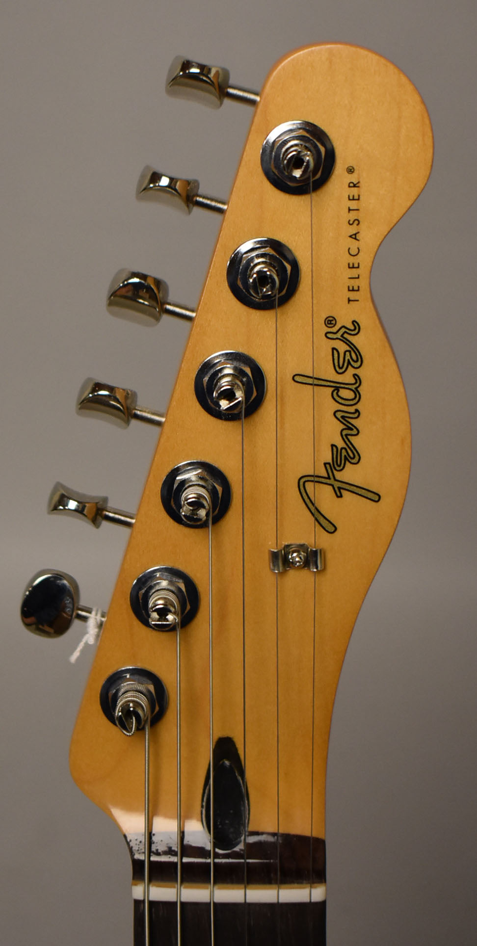 Close-up of the headstock, angled to the right, showing six chrome tuners, a string tree, and a dark truss rod cover.