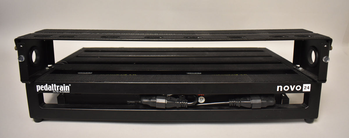 A black metal pedalboard with a slatted top surface and an open space underneath, viewed from the front, showing cables tucked below.