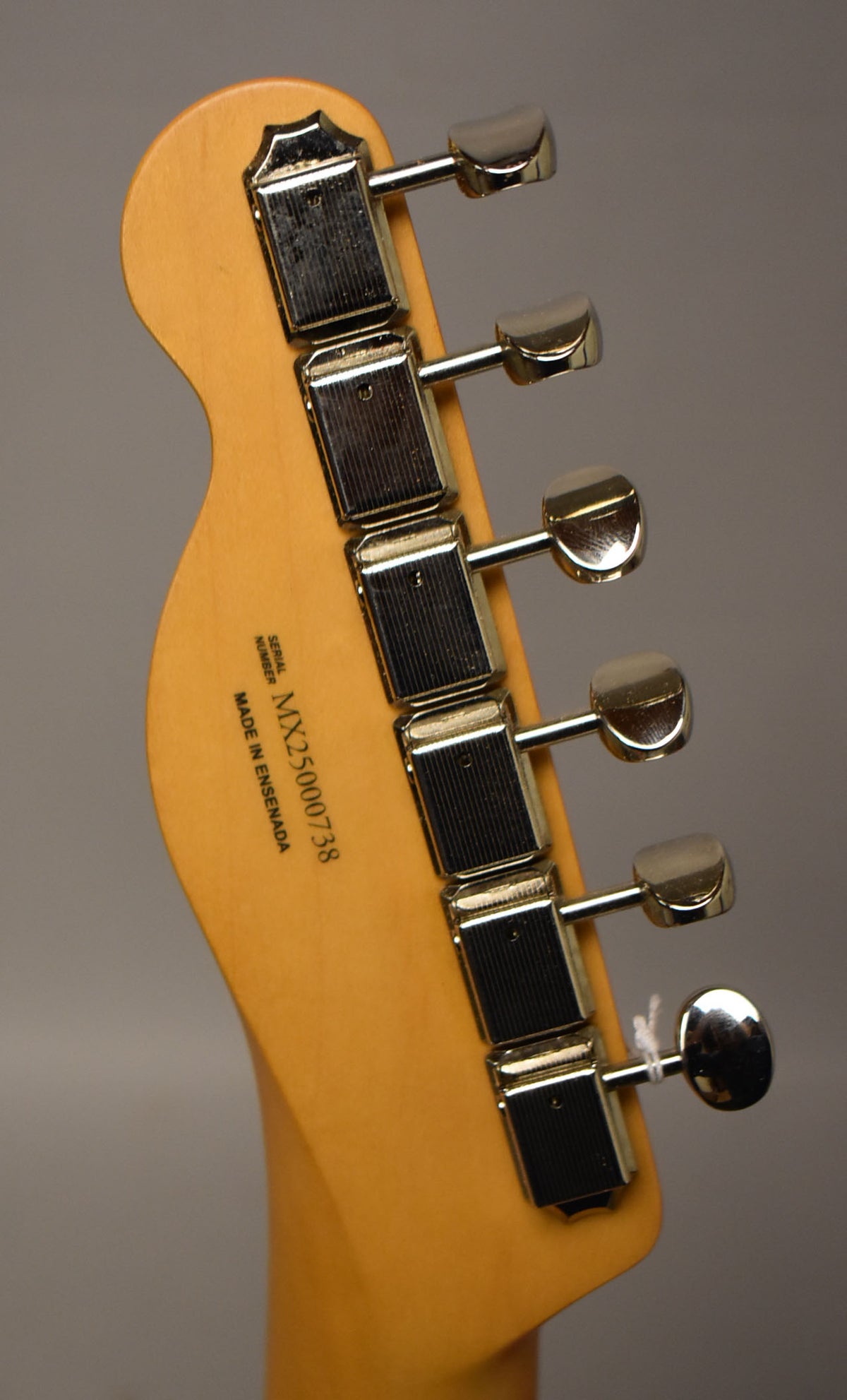 The back of a light blonde Telecaster headstock with six chrome tuners, angled left, showing some light wear.