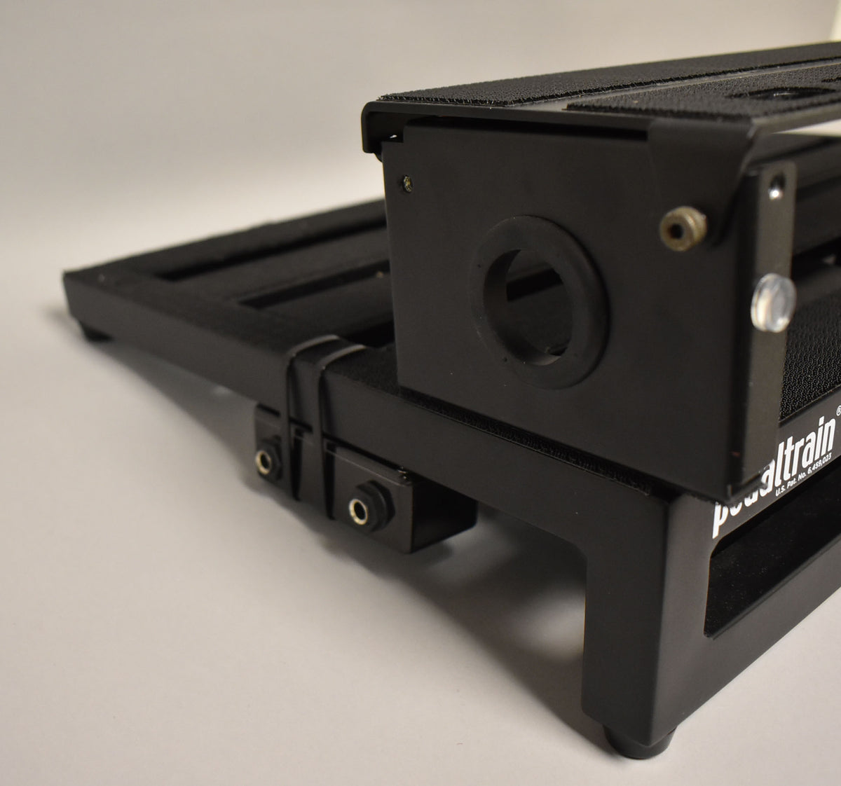 Close-up of the black pedalboard's right side, showing two input jacks, a circular cutout, and a clear plastic knob.