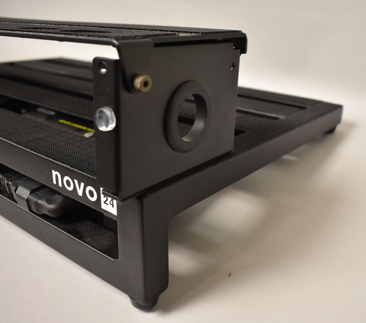 Close-up of the black pedalboard's right side, showing a circular cable grommet and a clear plastic foot.