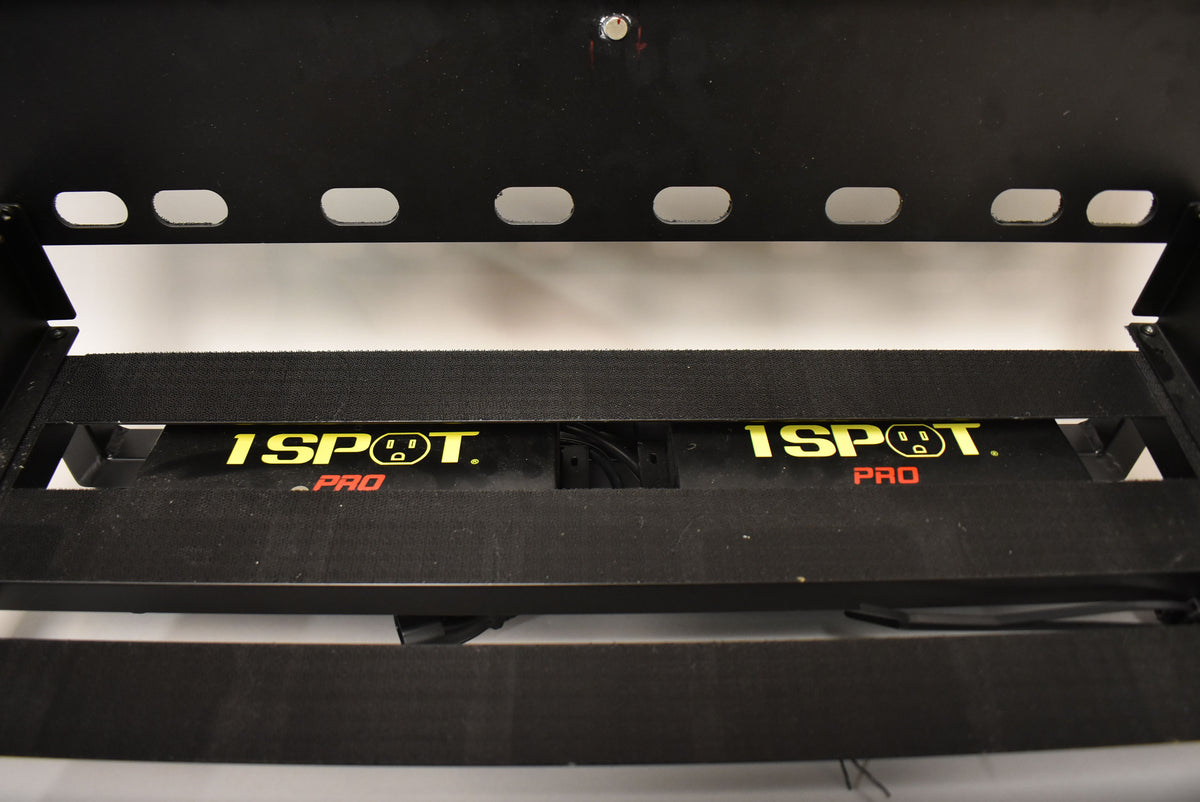 Close-up of the black pedalboard's underside, showing two yellow "1 SPOT PRO" power supply units mounted between the rails.