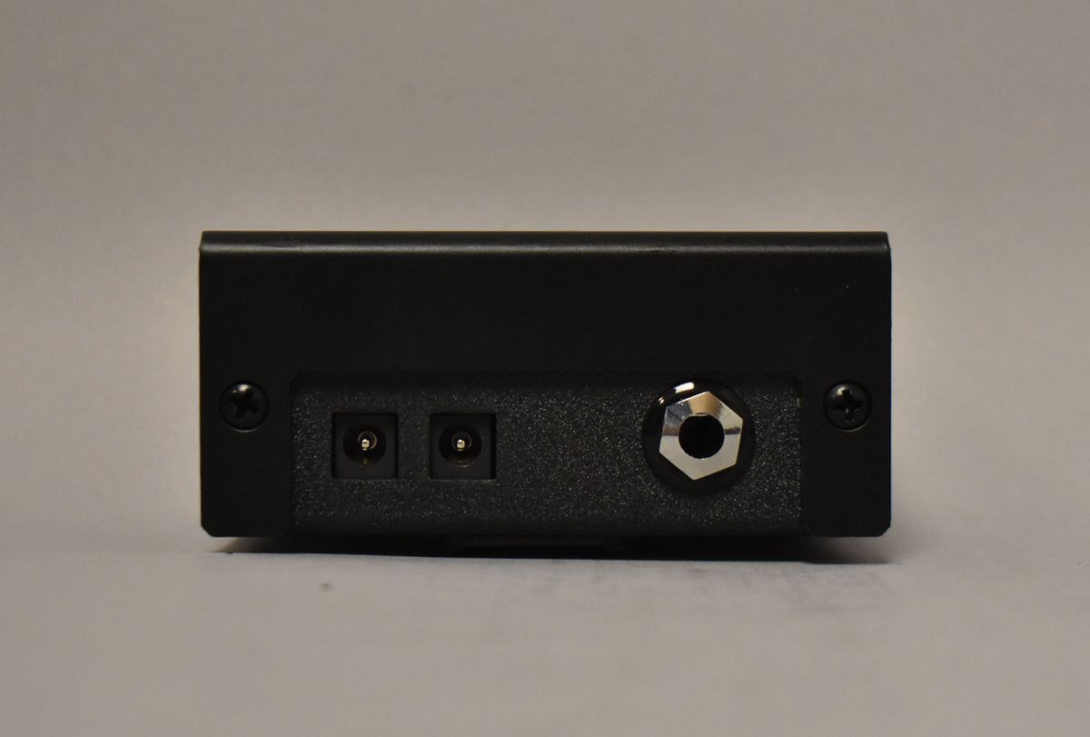 The black pedal's rear panel shows two power inputs and one chrome-ringed 1/4-inch jack, secured by four black screws.