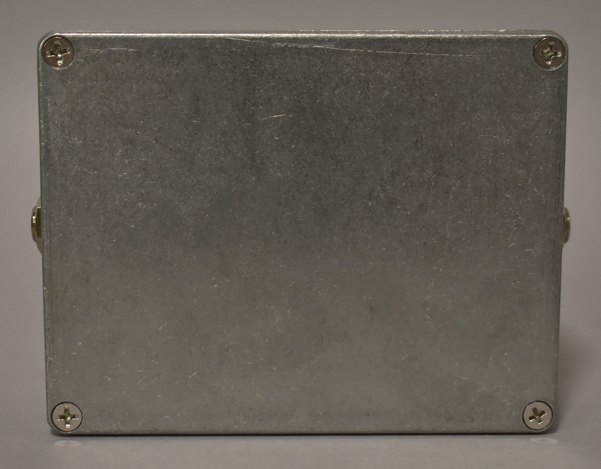 The effect pedal's brushed aluminum bottom plate is visible, secured by four Phillips head screws, with light surface scratches.