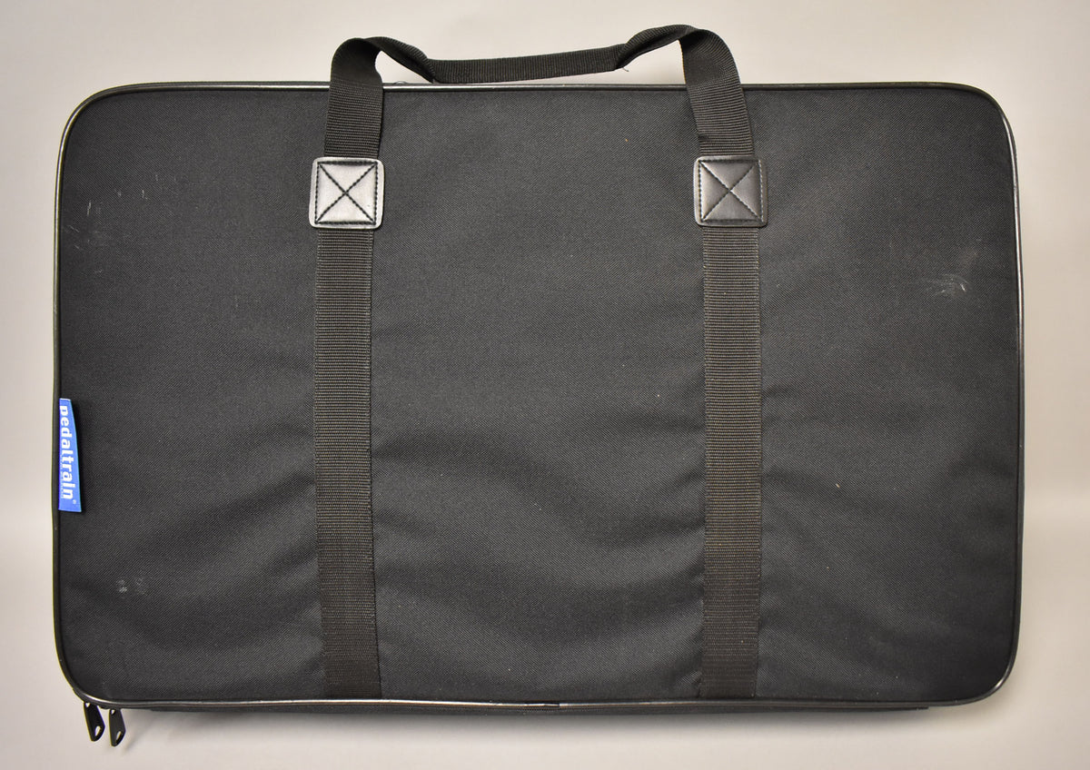 The black soft case for the pedalboard is shown from above, with two black straps and a carry handle visible.