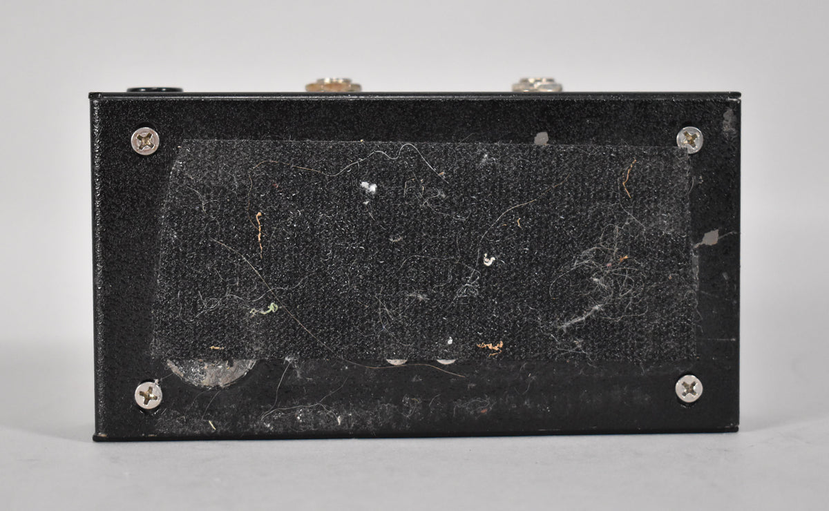 The pedal's black textured underside is covered in a worn, dusty black velcro pad, secured by four silver screws.