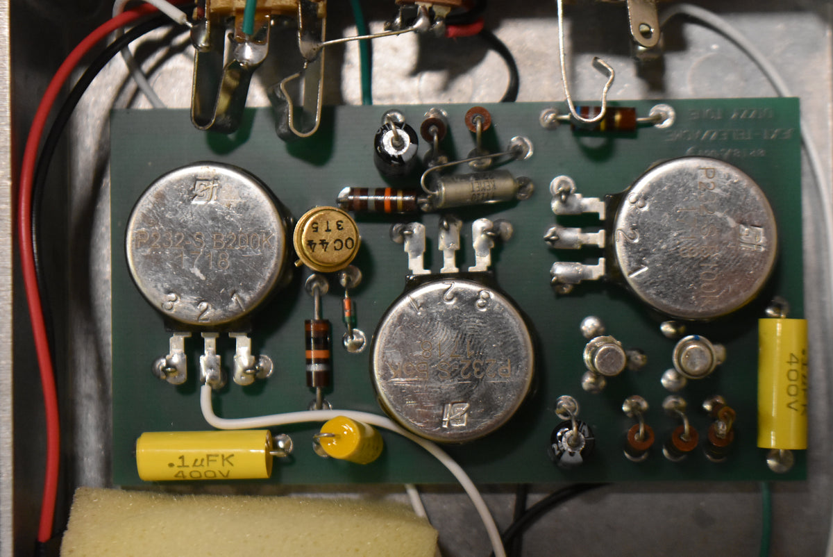 Overhead view of the pedal's internal circuit board, showing three large silver potentiometers, various resistors, and yellow capacitors.