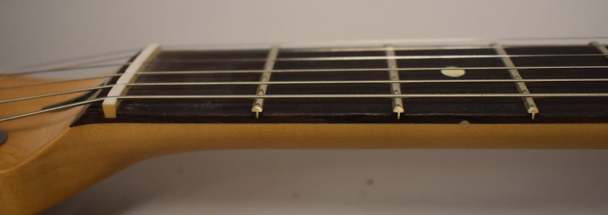 Close-up of the guitar's fretboard and nut, showing the light-colored nut, dark fretboard, and light maple neck.