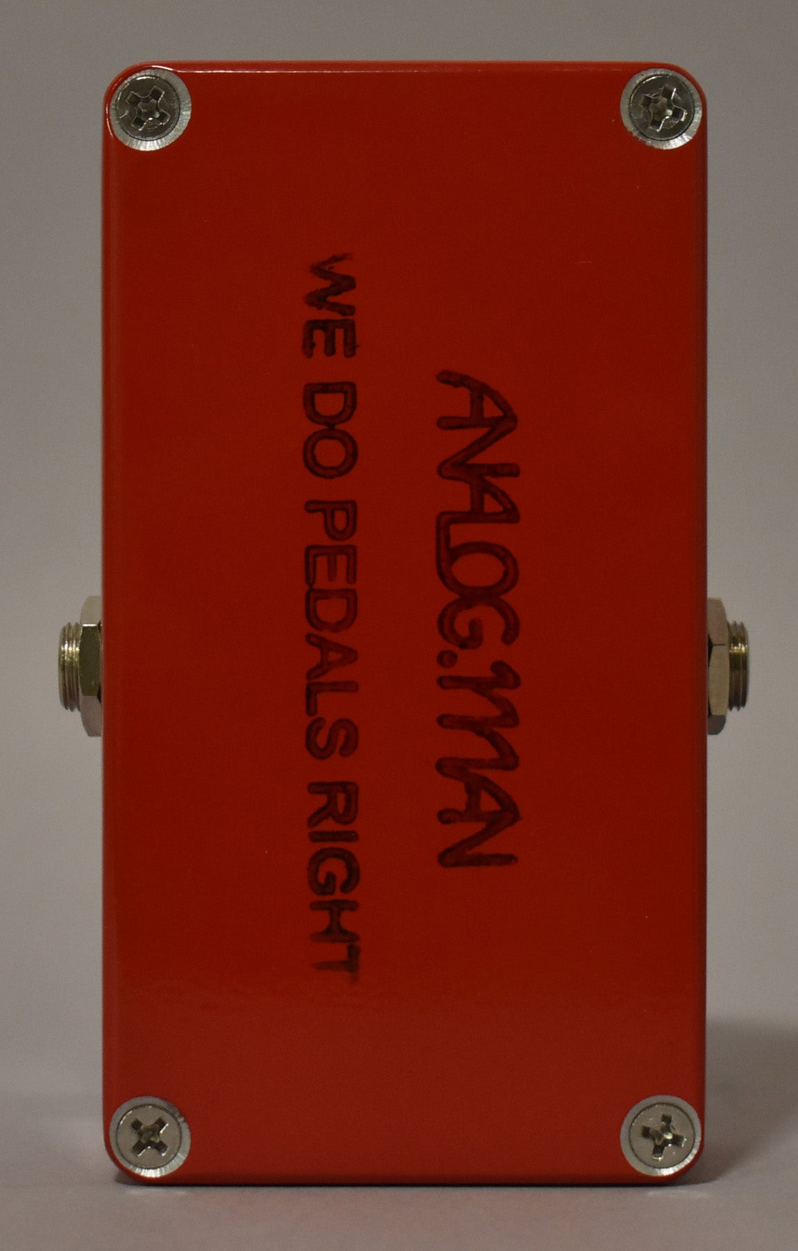 The red fuzz pedal is viewed from the bottom, showing four silver screws and two silver input jacks on the sides.