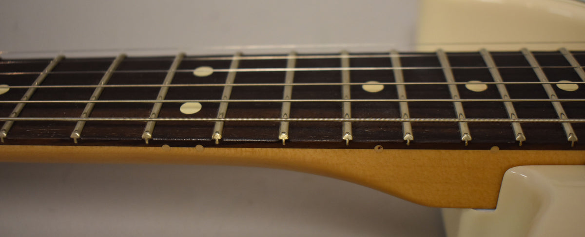 Close-up of the guitar's dark fretboard with light dot inlays, showing frets and strings, and the light blonde neck.
