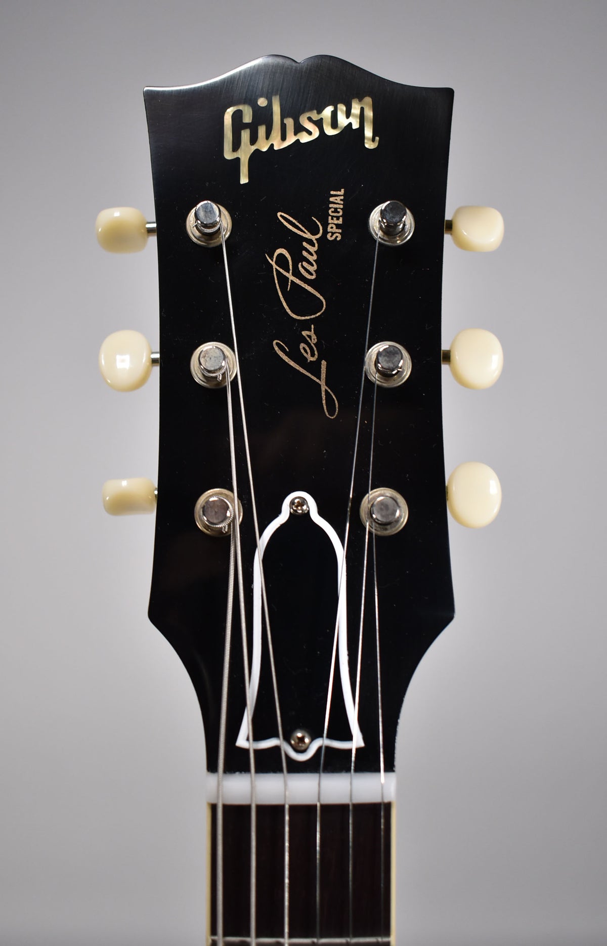 Close-up of the black headstock with cream tuners, showing the bell-shaped truss rod cover and light finish checking.