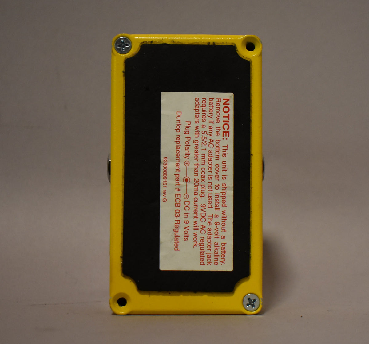 The yellow pedal is seen from the bottom, revealing a black base plate with a white warning sticker.