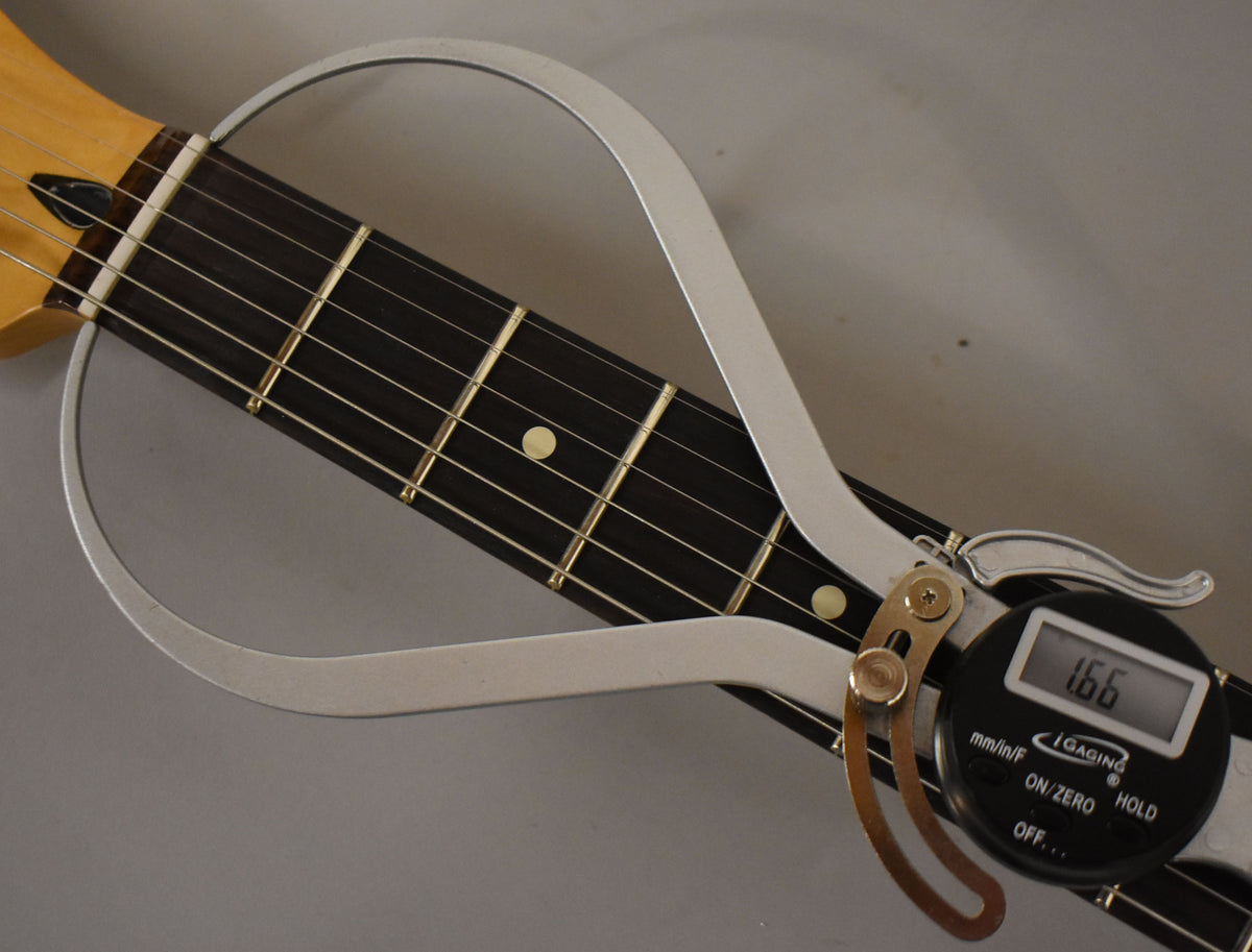 Close-up of the guitar's dark fretboard and light maple neck, with a silver digital fret rocker showing a 1.66mm reading.