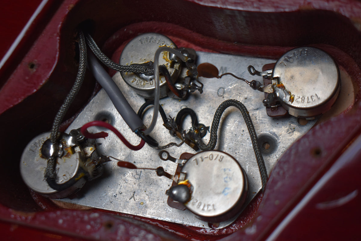 Close-up of the guitar's control cavity, revealing four pots, wiring, and capacitors, with some visible solder oxidation.